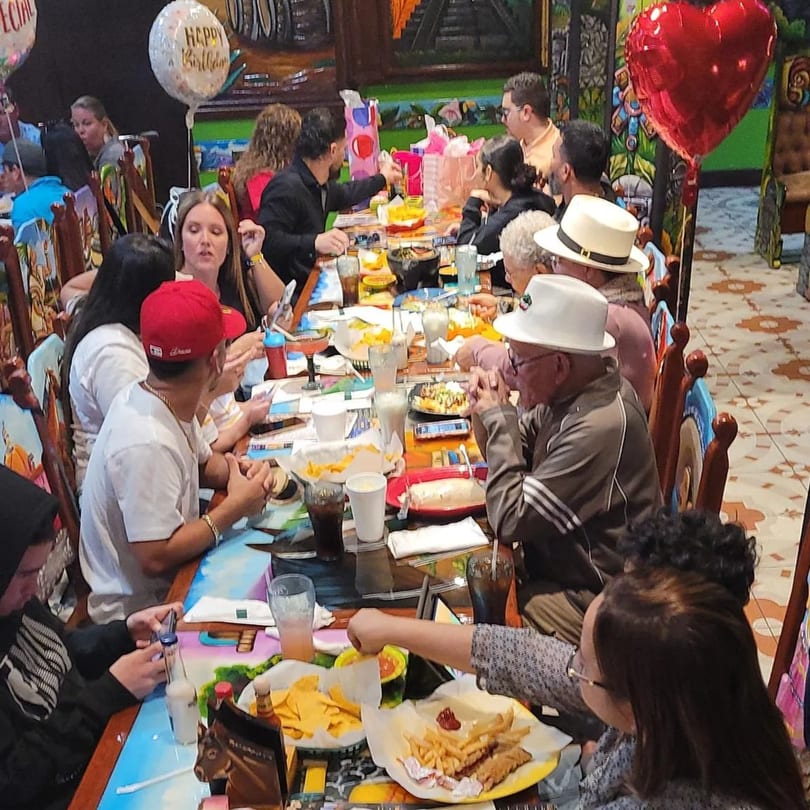 A large group of people celebrating a birthday at a vibrant Mexican restaurant, enjoying food and drinks.