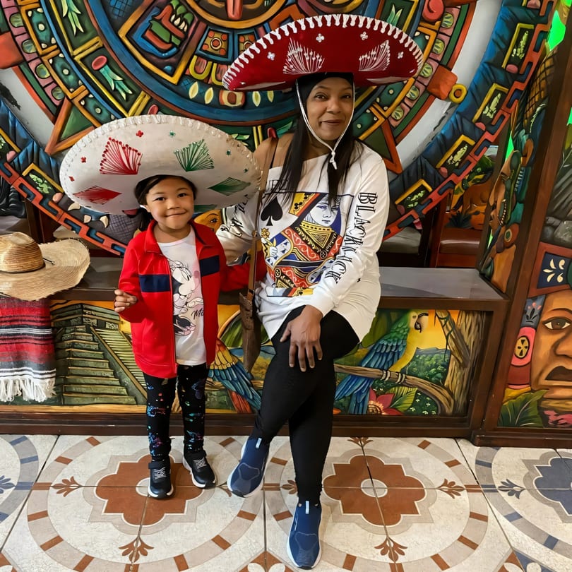 A woman and child wearing sombreros pose in front of a colorful Mexican-themed mural at Fiesta Cancún.