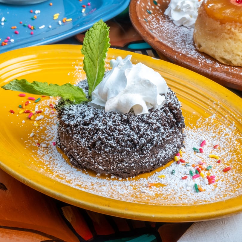 Chocolate lava cake with whipped cream, mint, powdered sugar, and sprinkles on a yellow plate.