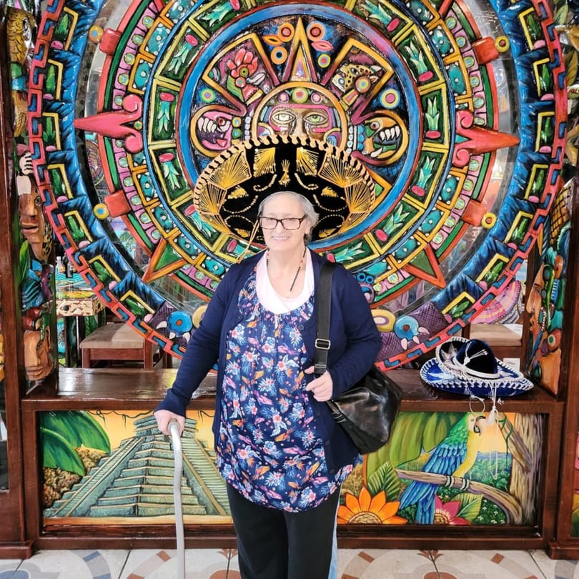 A woman in a sombrero stands in front of a colorful Aztec calendar mural at Fiesta Cancún.